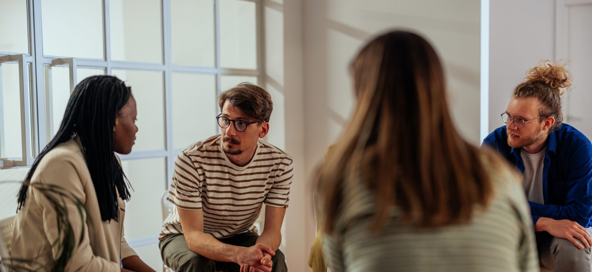 a group of people are sitting inside in a circle of chairs and are engaged in a discussion